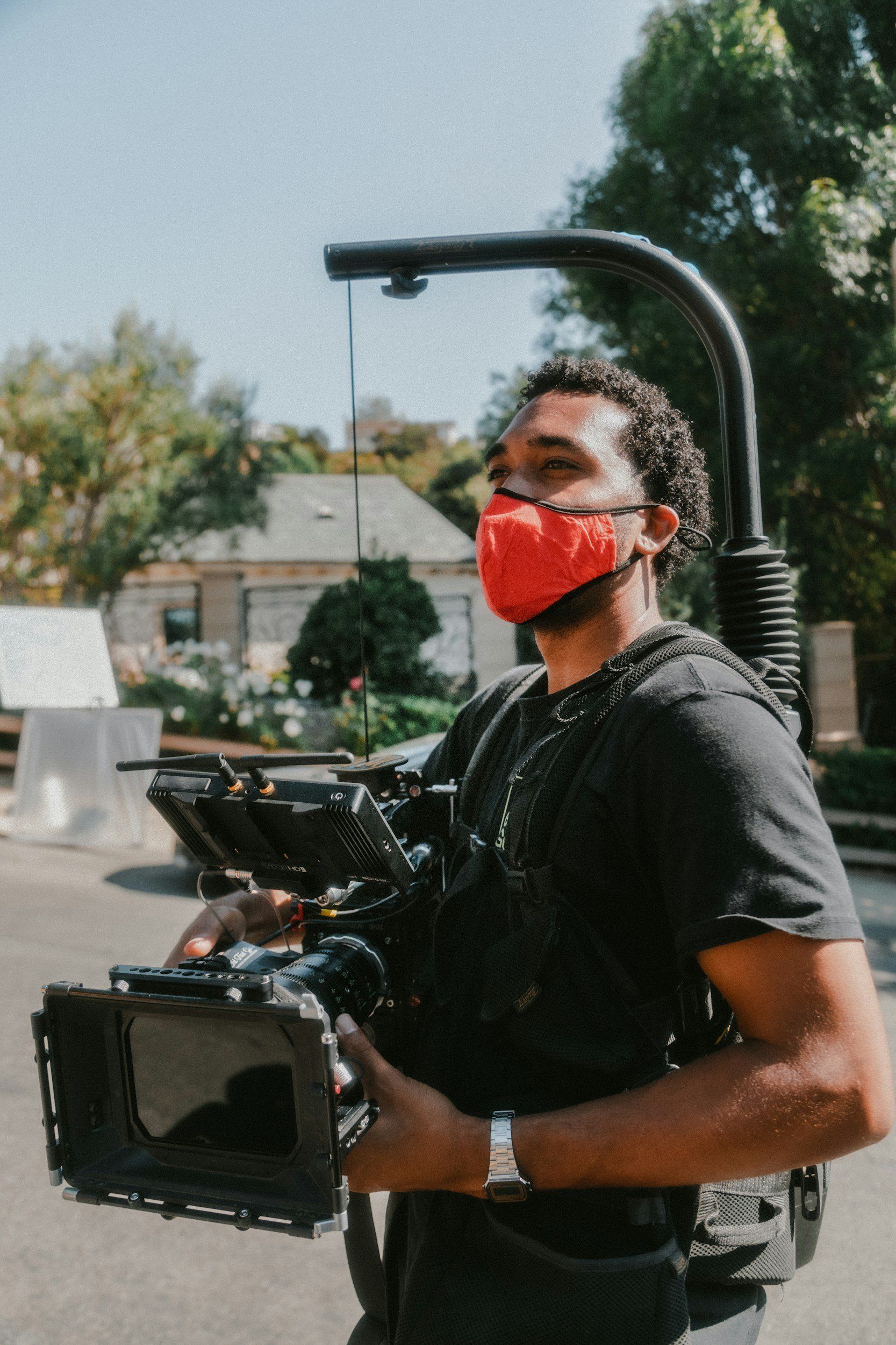 A man wearing a red mask is holding a camera.
