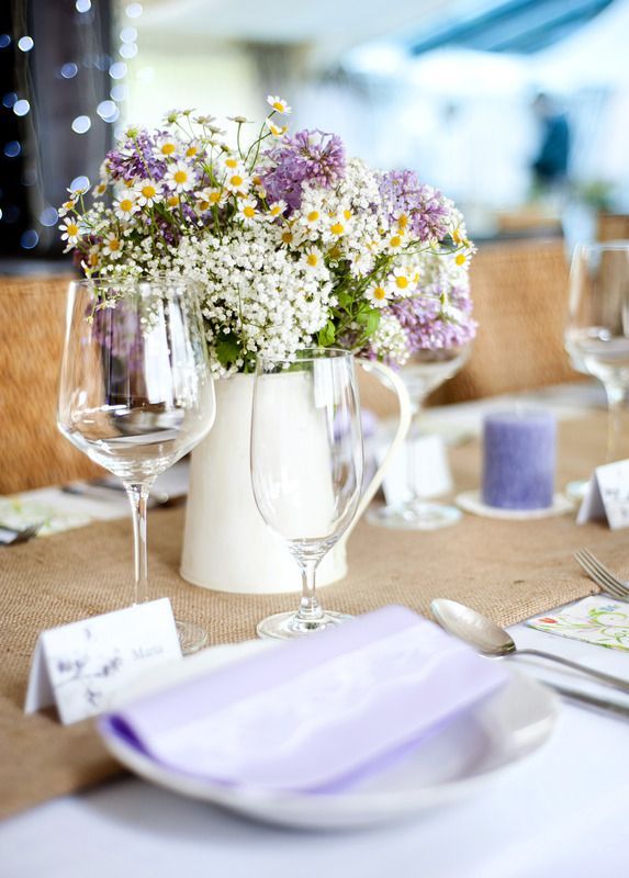 A table set for a wedding reception with a pitcher filled with flowers and wine glasses.