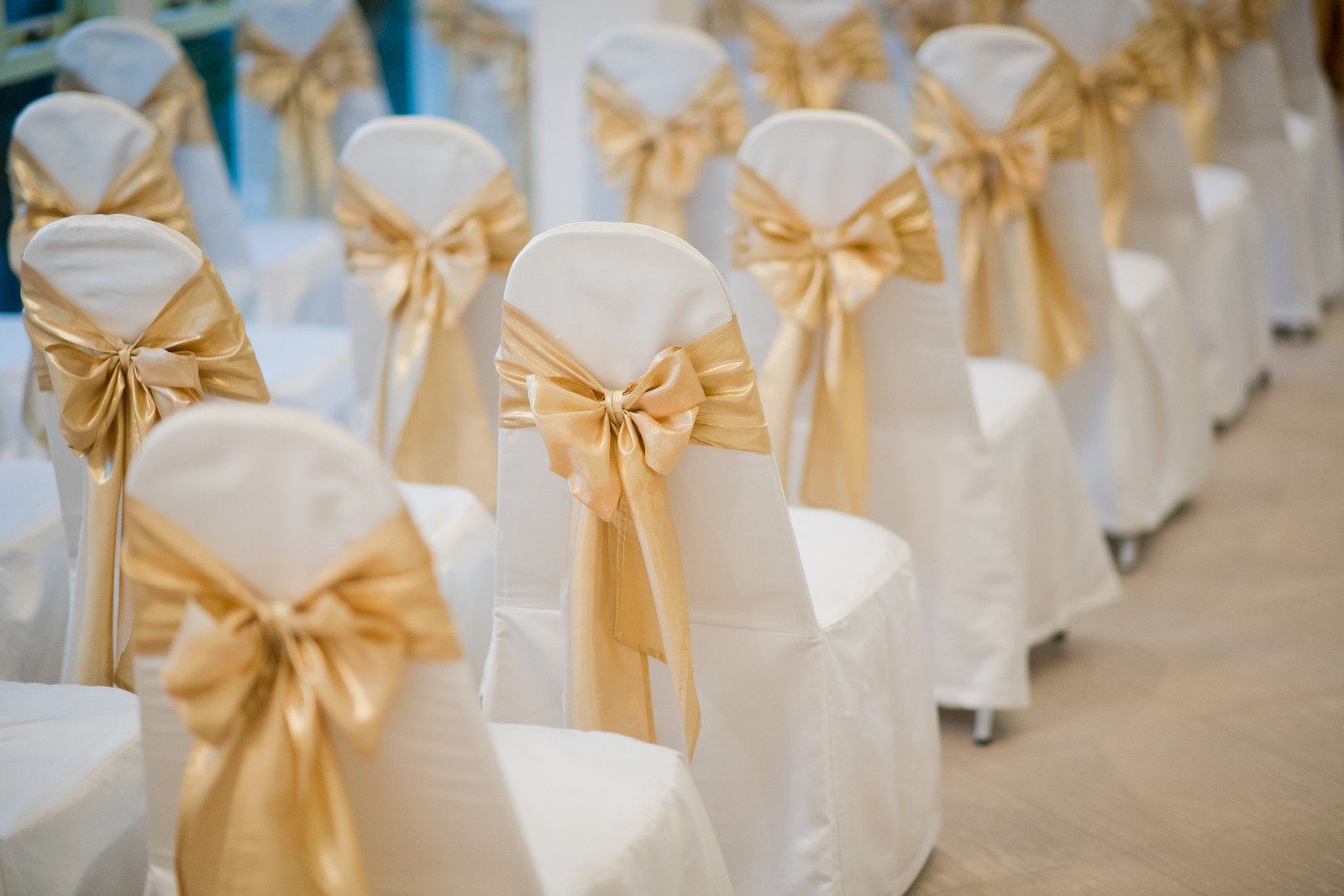 A row of white chairs with gold bows on them.