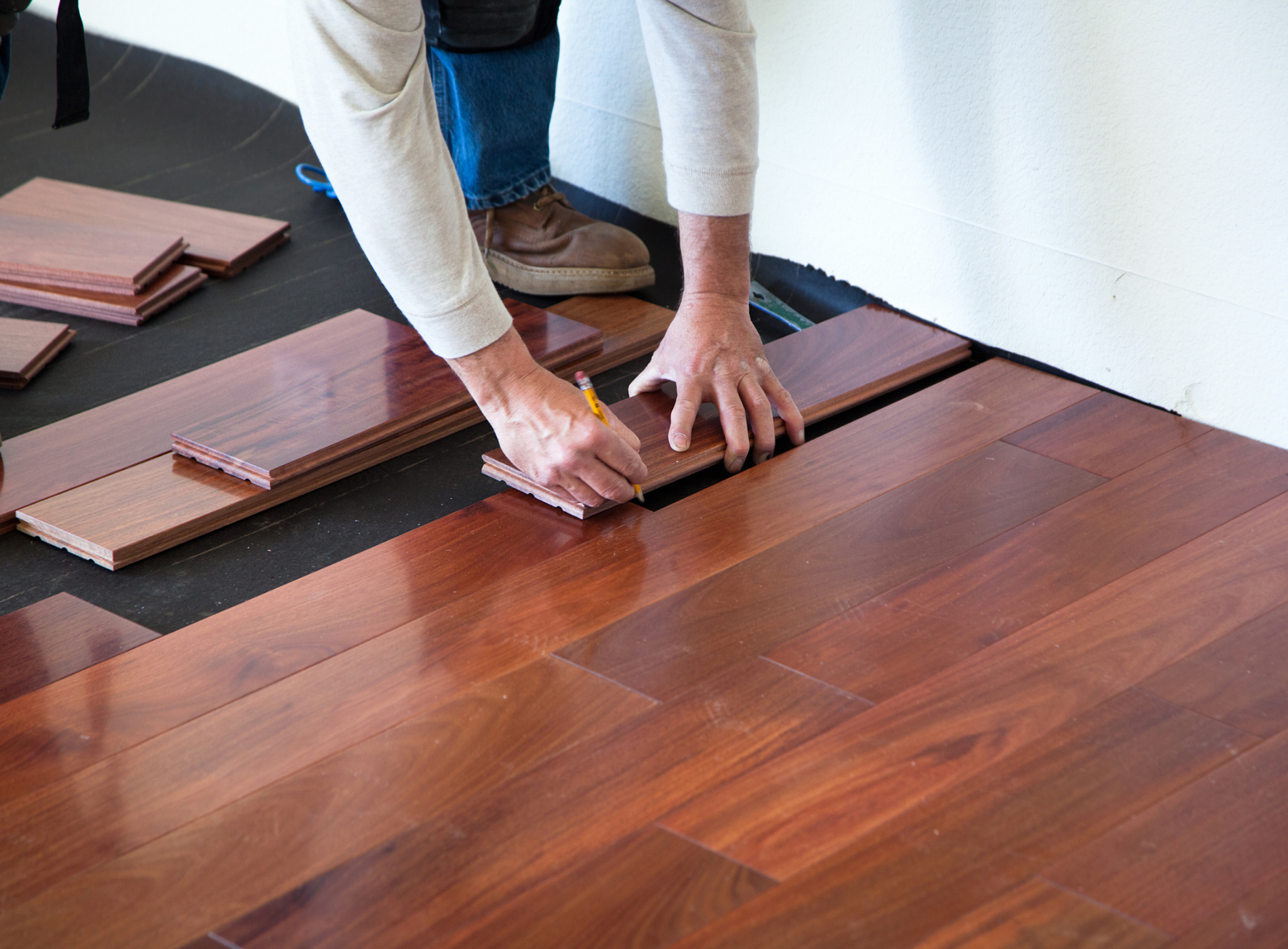 A person is measuring a piece of wood on a hardwood floor.