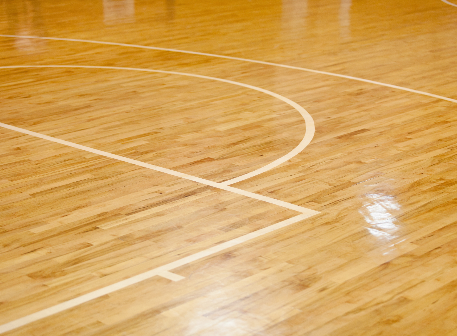 A wooden basketball court with a white line on it.