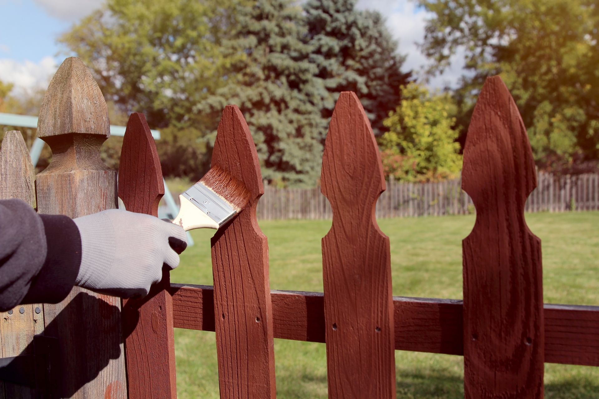 A person is painting a wooden fence with a brush.