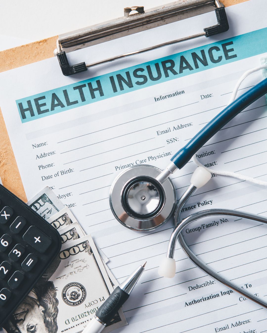 Health insurance form with stethoscope, calculator, and dollar bill on a clipboard