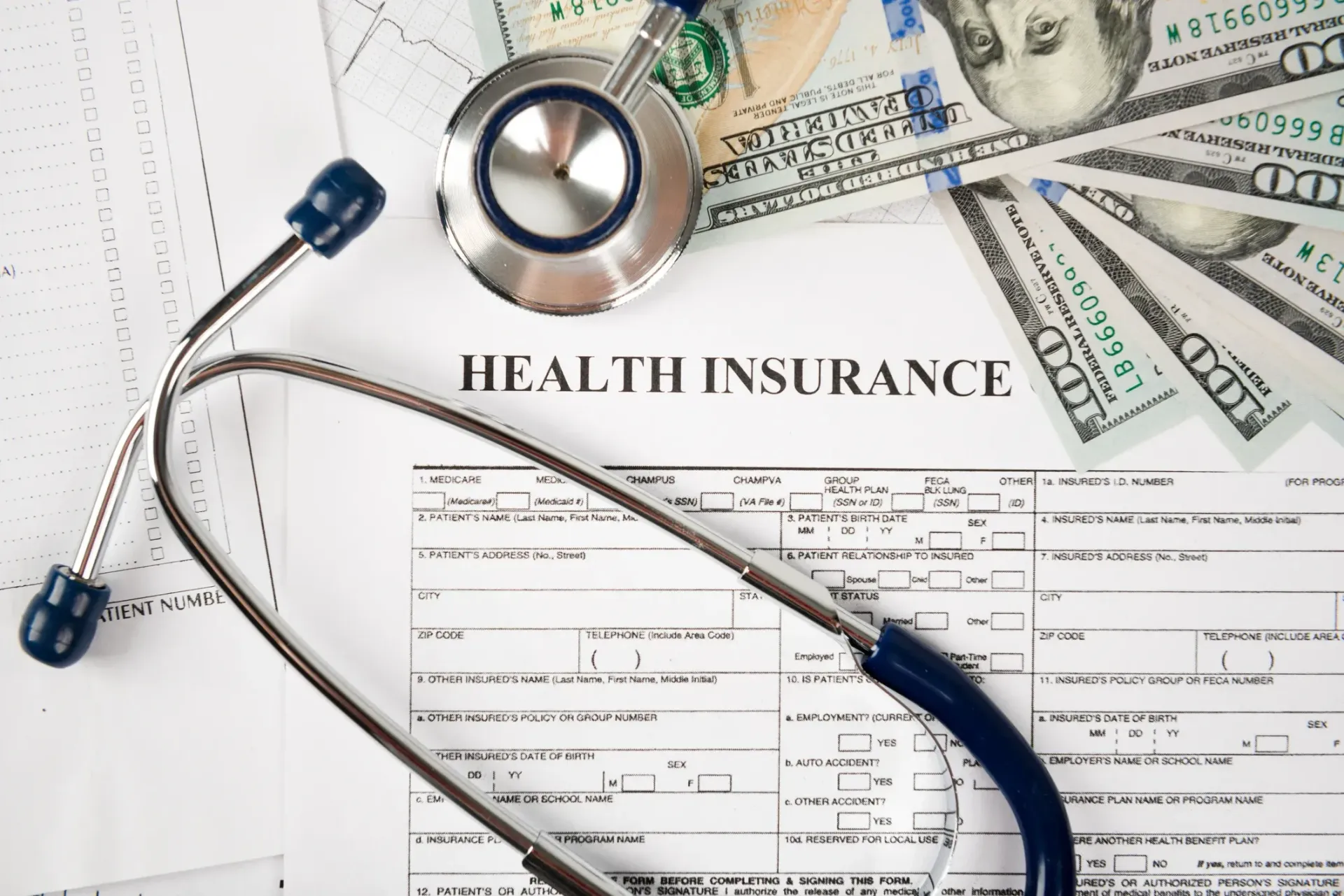 Stethoscope, health insurance forms, and cash on a desk