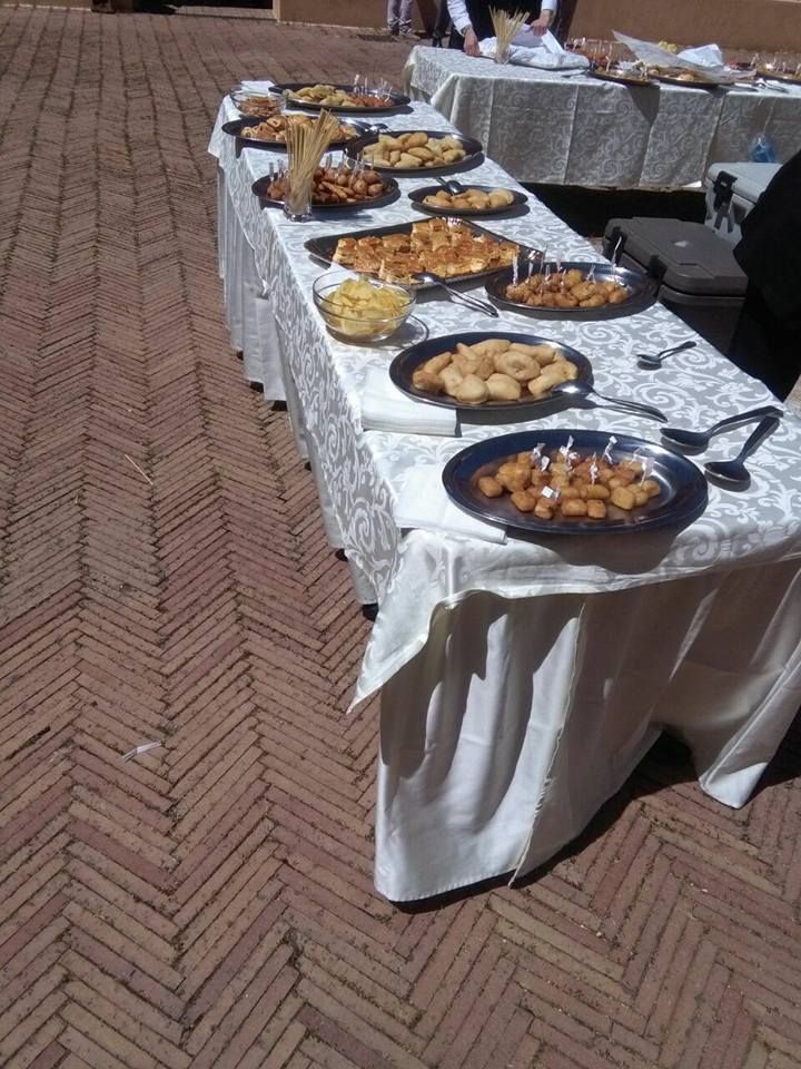 Un tavolo imbandito con vari antipasti durante un evento all'aperto, disposto su una pavimentazione in mattoni.