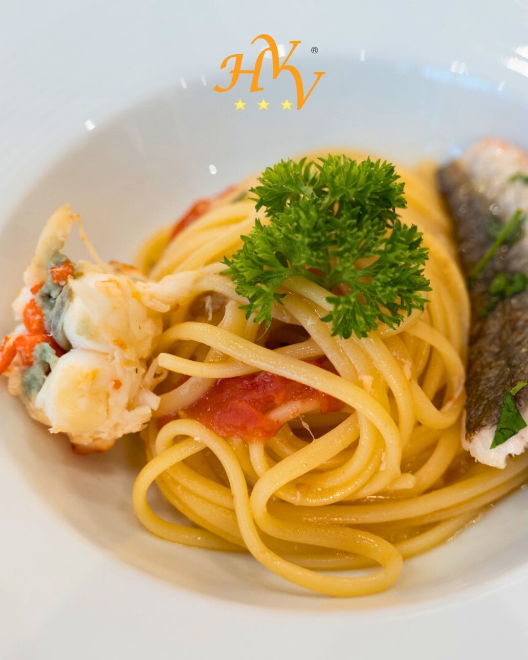 Linguine con gamberi, salsa di pomodoro, filetto di pesce, guarnite con prezzemolo su un piatto bianco.