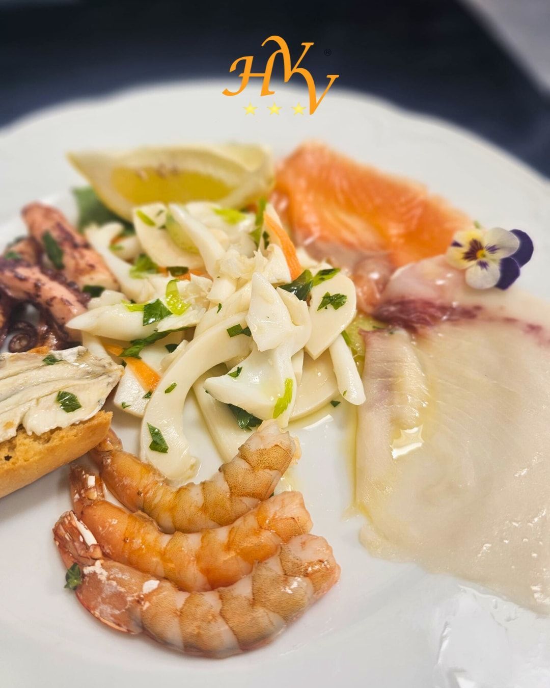 Antipasto di mare su piatto bianco: gamberi, insalata di calamari, pesce, salmone, polpo e uno spicchio di limone.