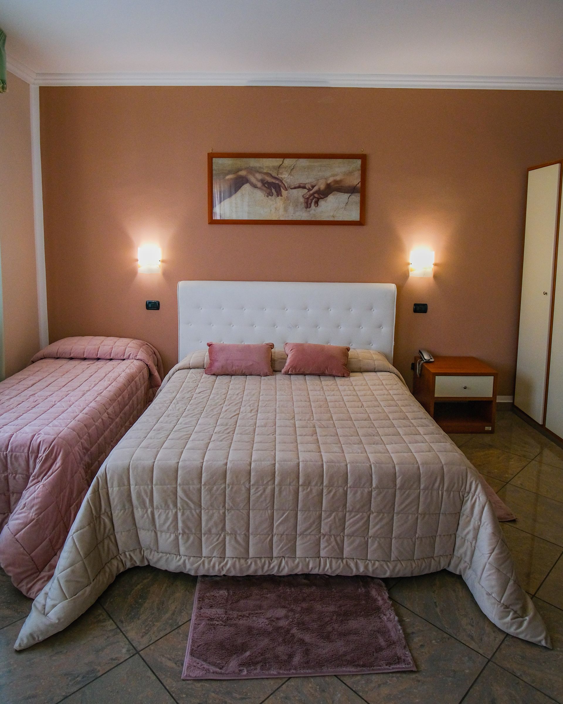 Camera da letto con letto matrimoniale, letto singolo e opere d'arte su una parete rosso-marrone.