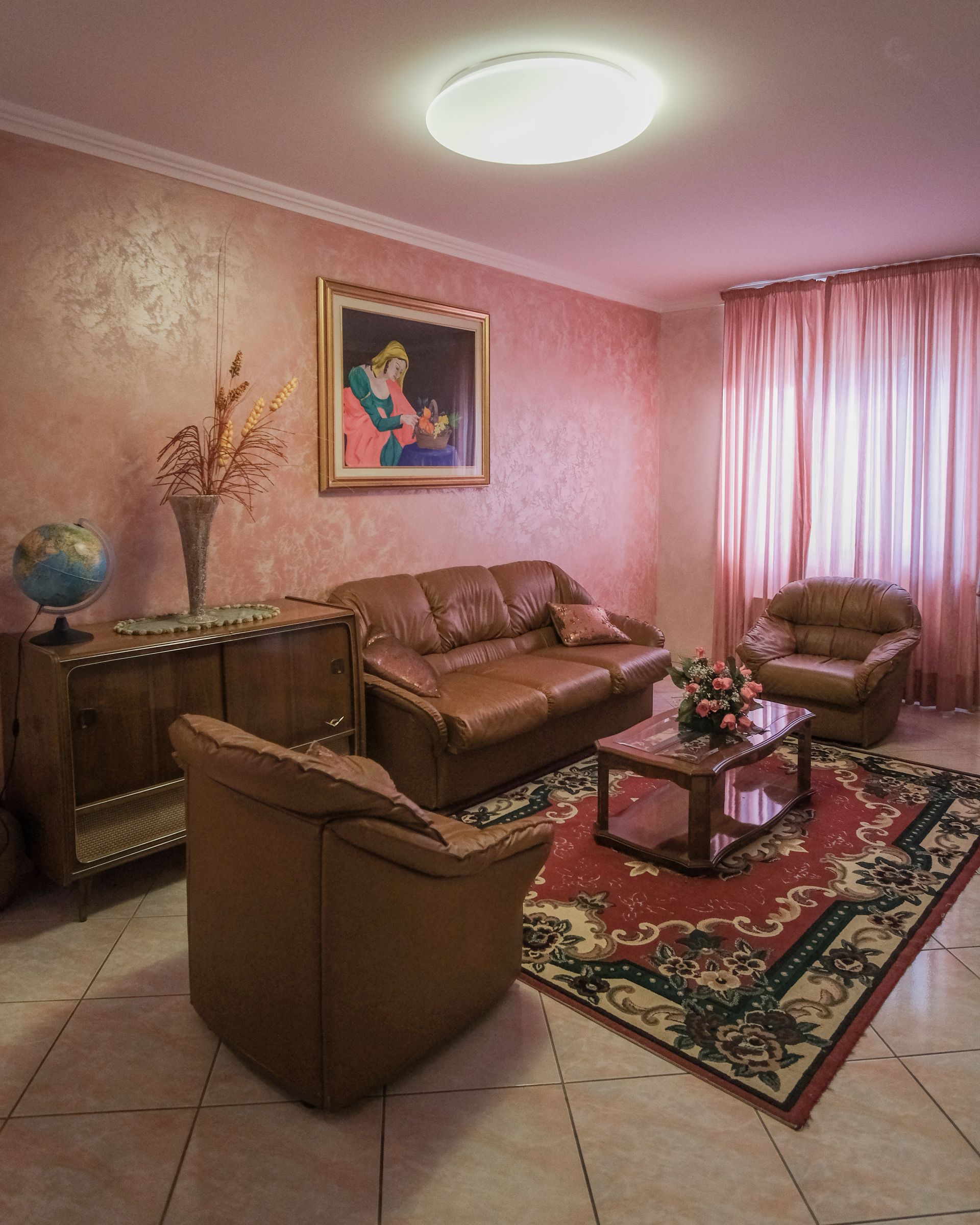 Soggiorno con mobili in pelle marrone, tappeto rosso, pareti rosa e un dipinto.