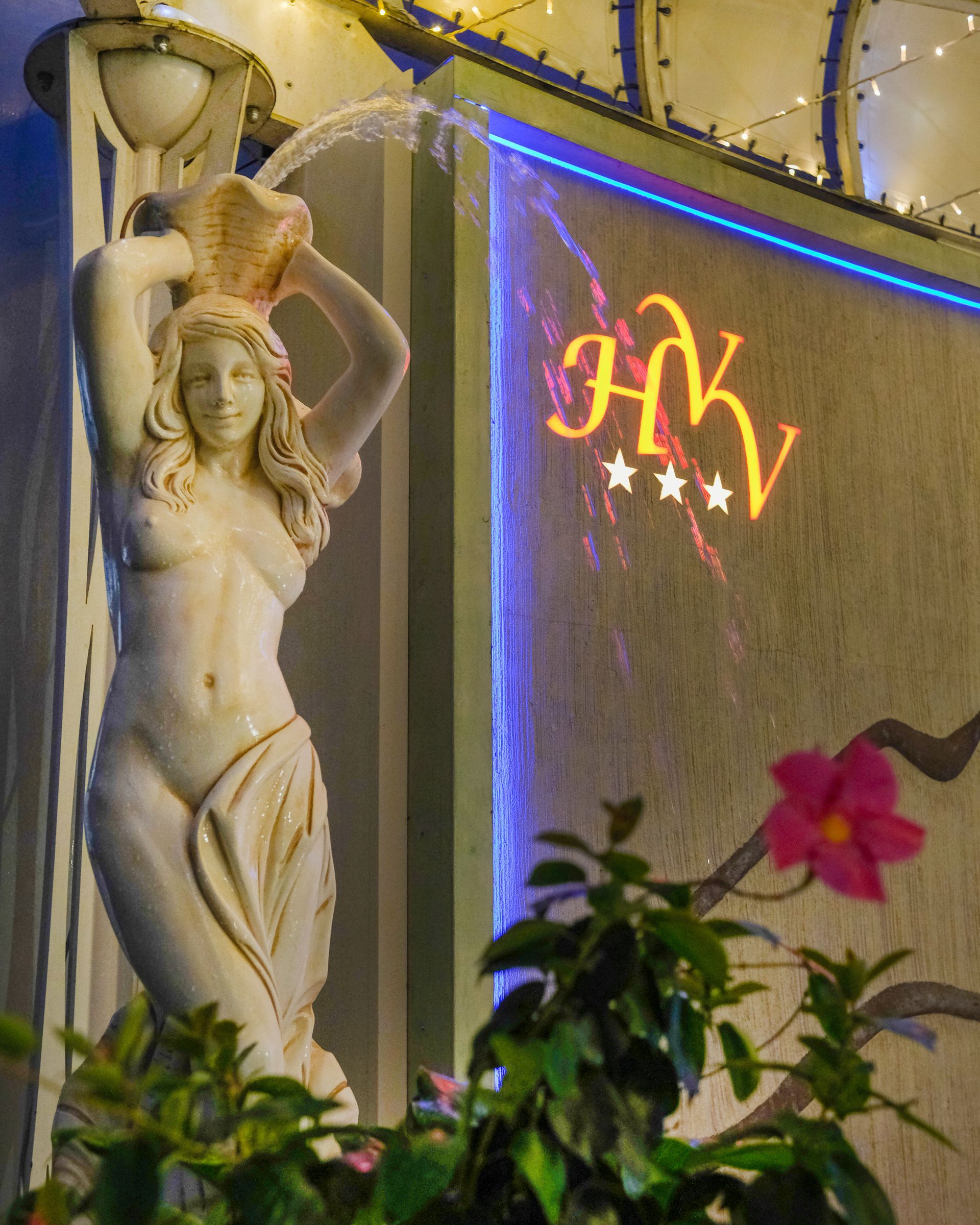 Statua di una donna che versa acqua, accanto a un'insegna luminosa con la scritta