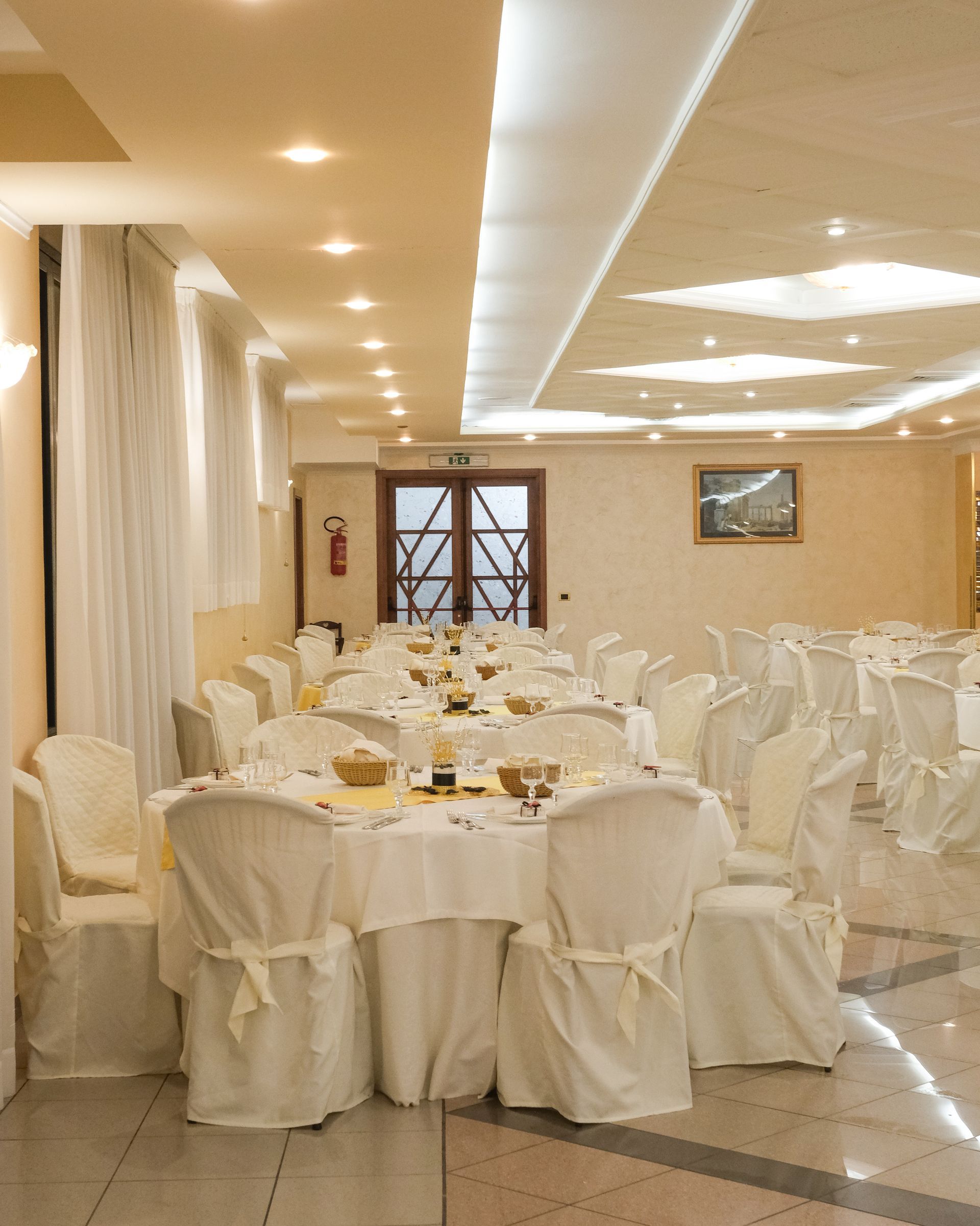Sala da pranzo formale con tavoli e sedie rivestiti di bianco. Illuminazione calda.
