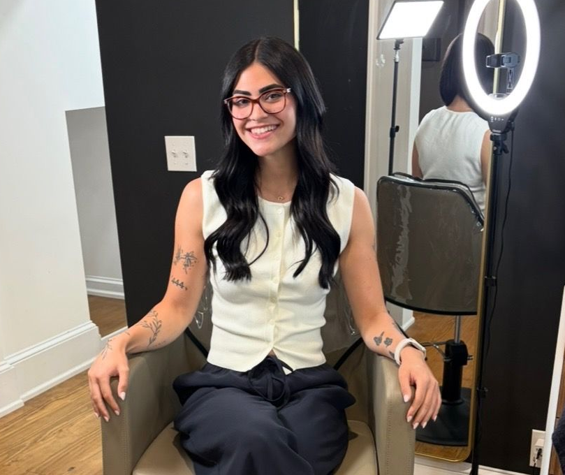 Woman in black scrubs smiles in front of a Roots sign, polka dot wall.