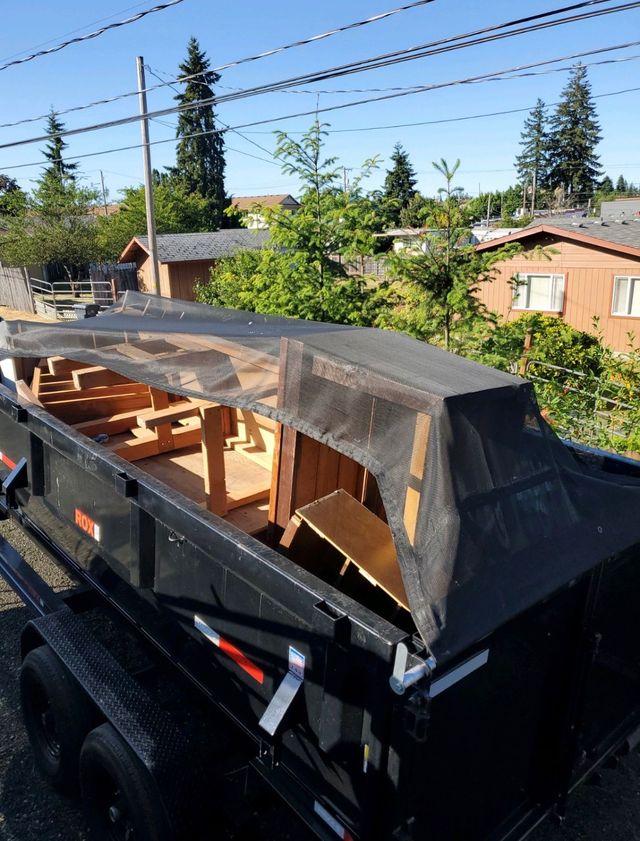 Black dumpster trailer with a wooden frame and netting on top, in a residential area.