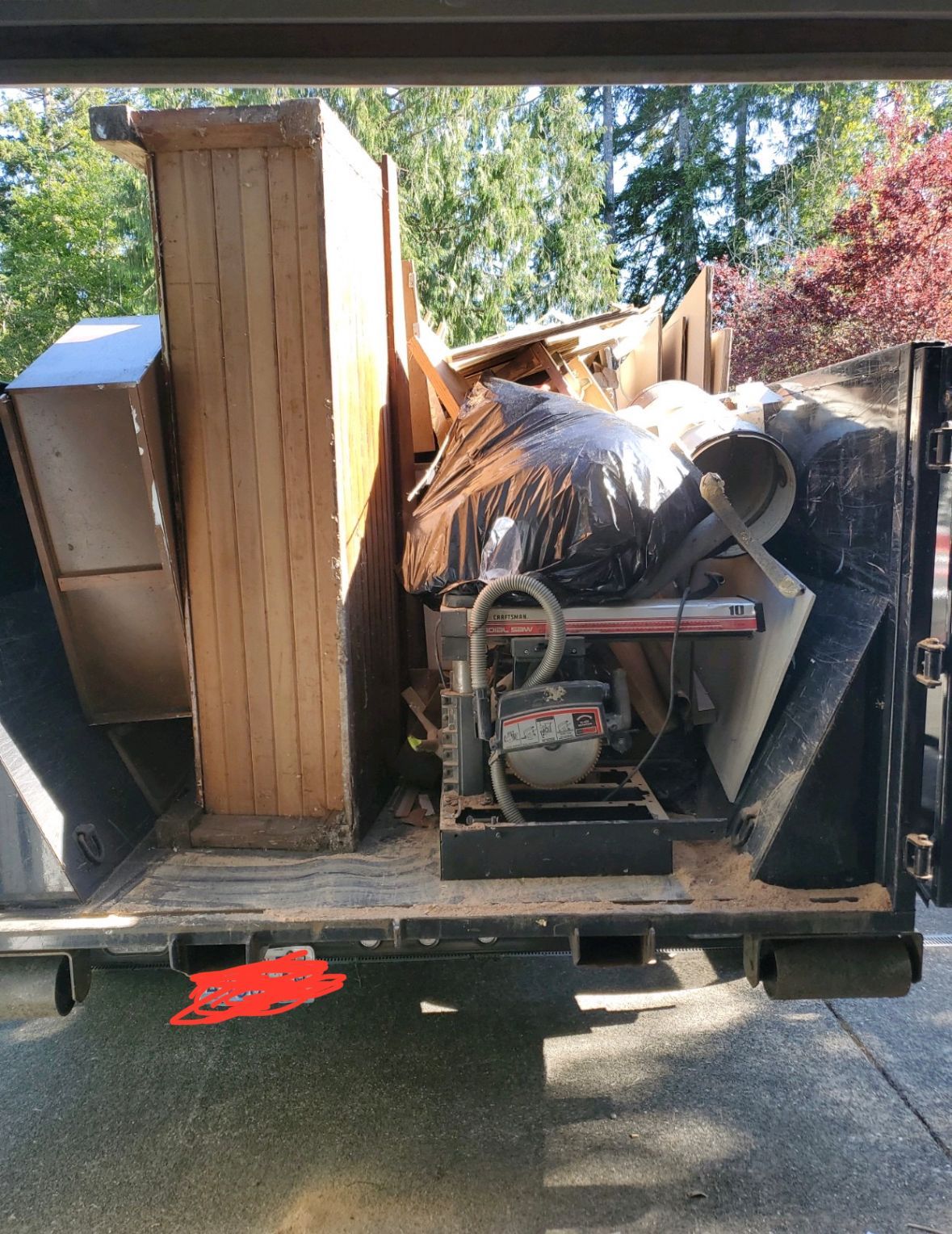 A truck bed filled with discarded furniture, a saw, and debris, outdoors in a yard.