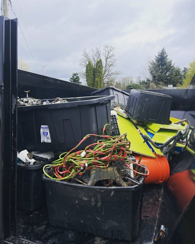 A truck bed full of debris, including black bins, cords, and a yellow item, against a cloudy sky.