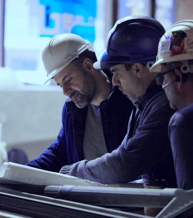 Three men wearing hard hats are looking at a blueprint