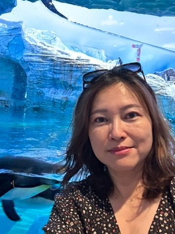 A woman wearing sunglasses is standing in front of a penguin tank.