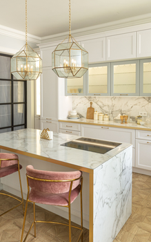 Bright white kitchen with marble island, gold pendant lights, and pink velvet barstool.