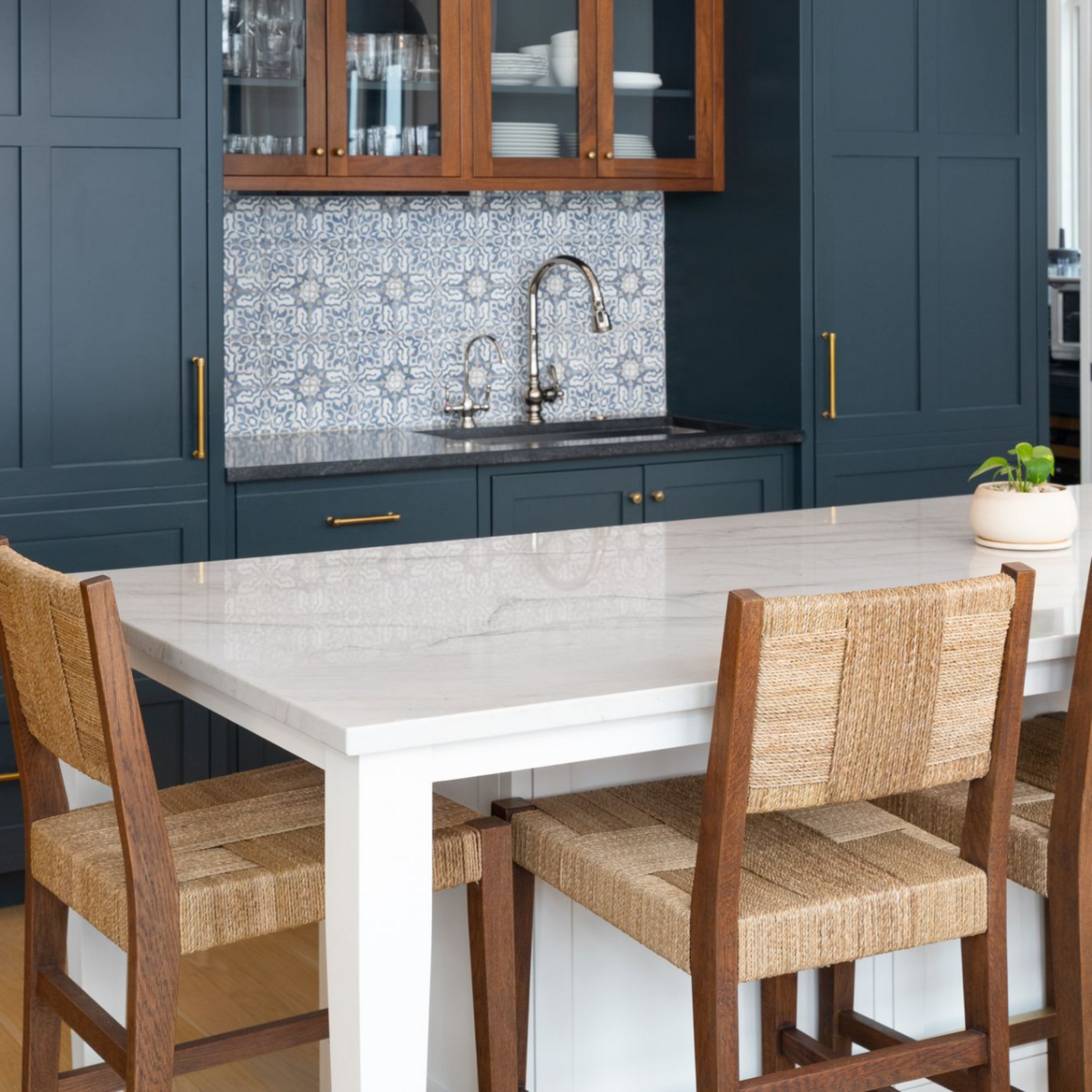 Modern kitchen with navy cabinets, patterned tile backsplash, and a white island with woven bar stools