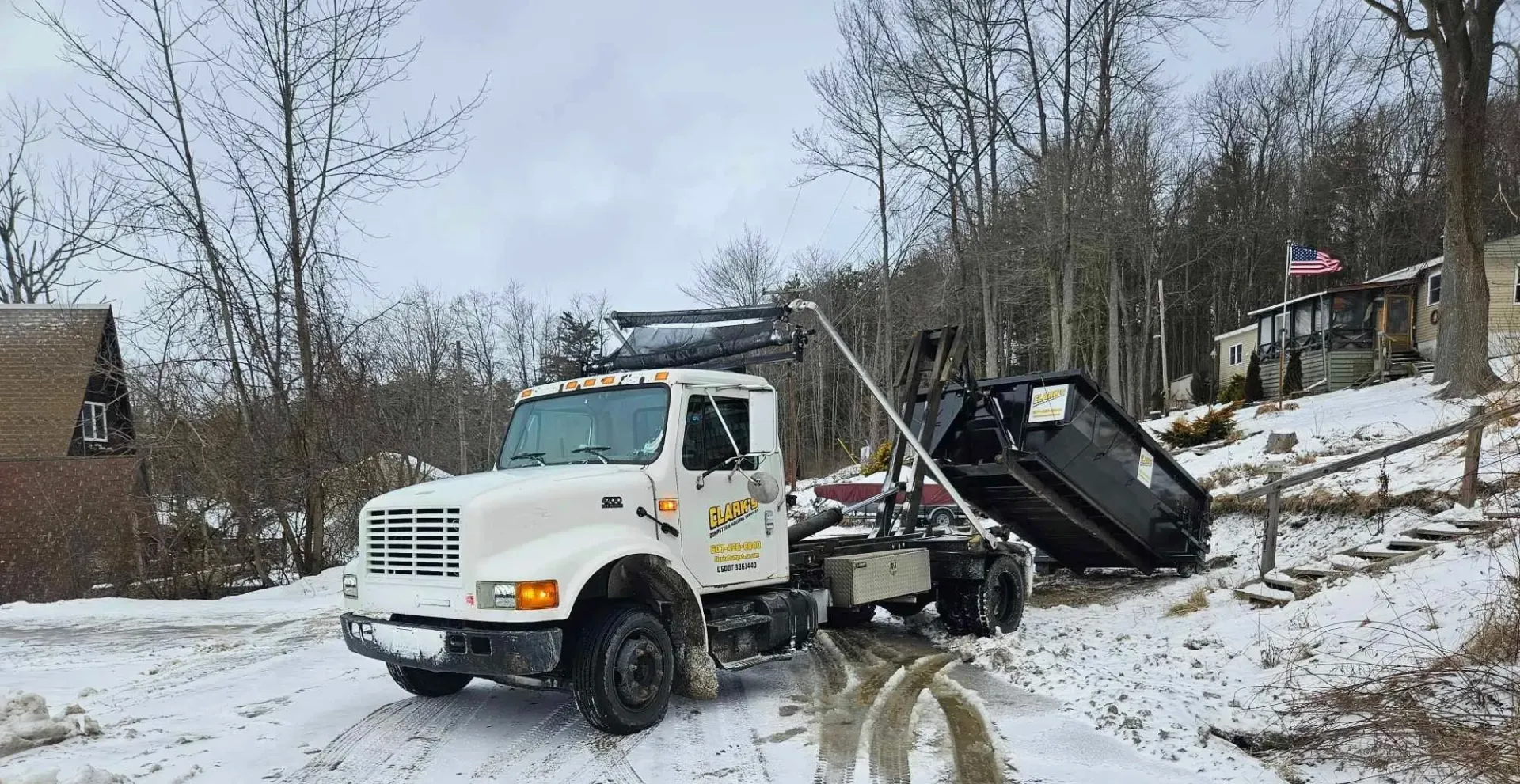 A dump truck is driving down a snowy road next to a house.