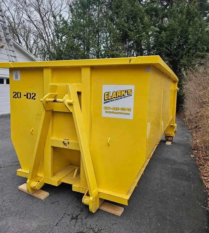 A large yellow dumpster is parked in front of a house under construction.