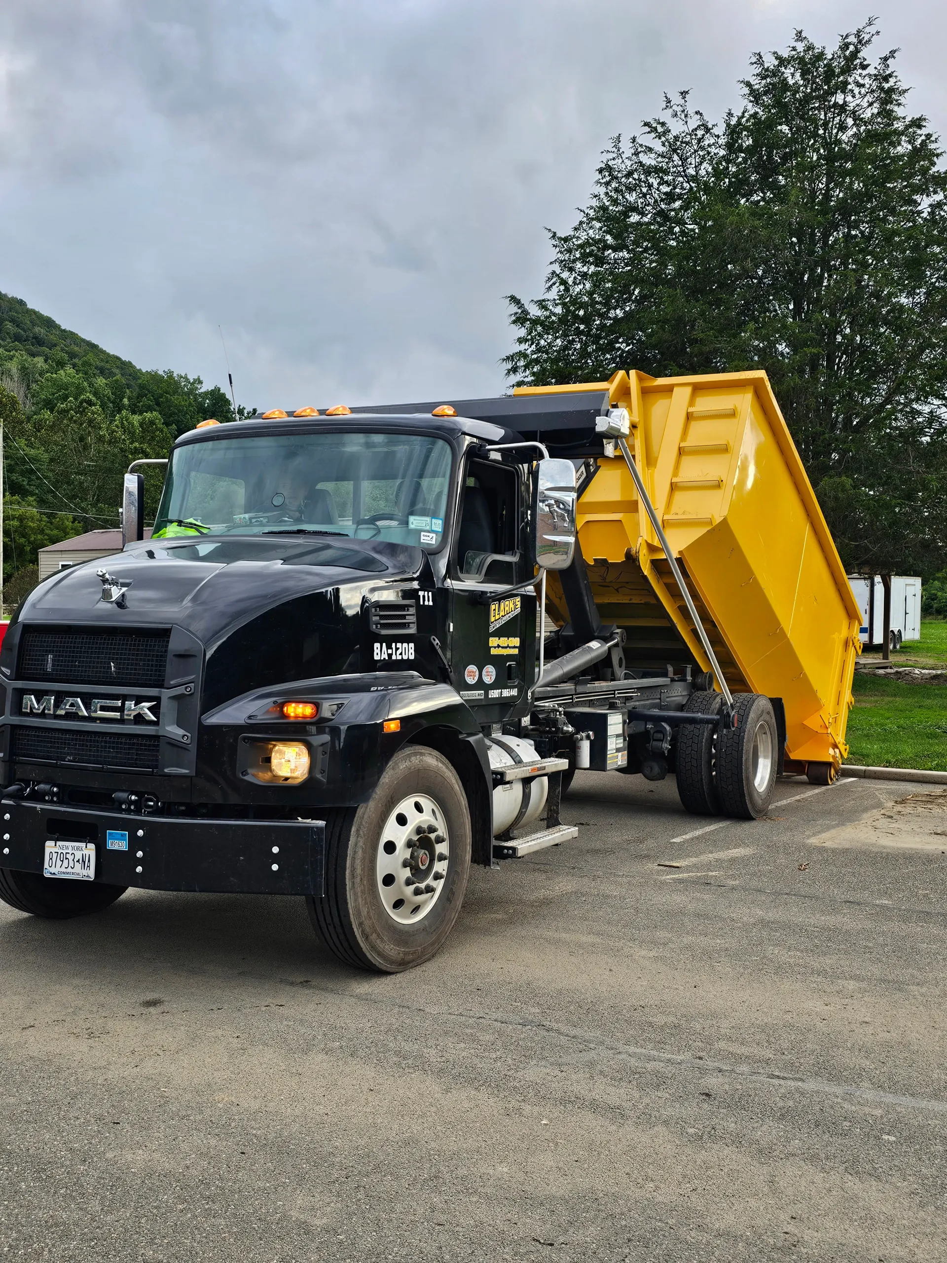 A black dump truck with a yellow dump trailer is parked in a gravel lot.