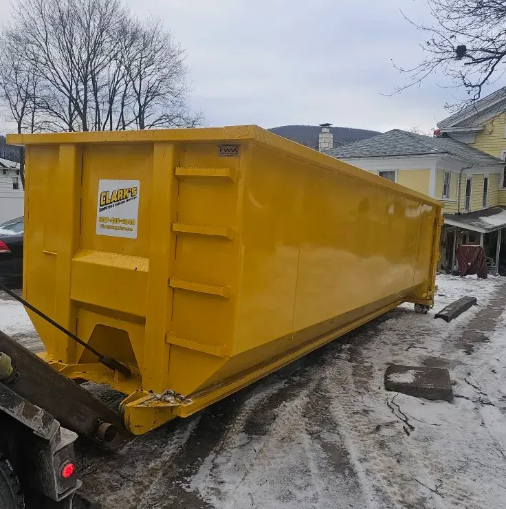 A large yellow dumpster is sitting in the snow in front of a house.