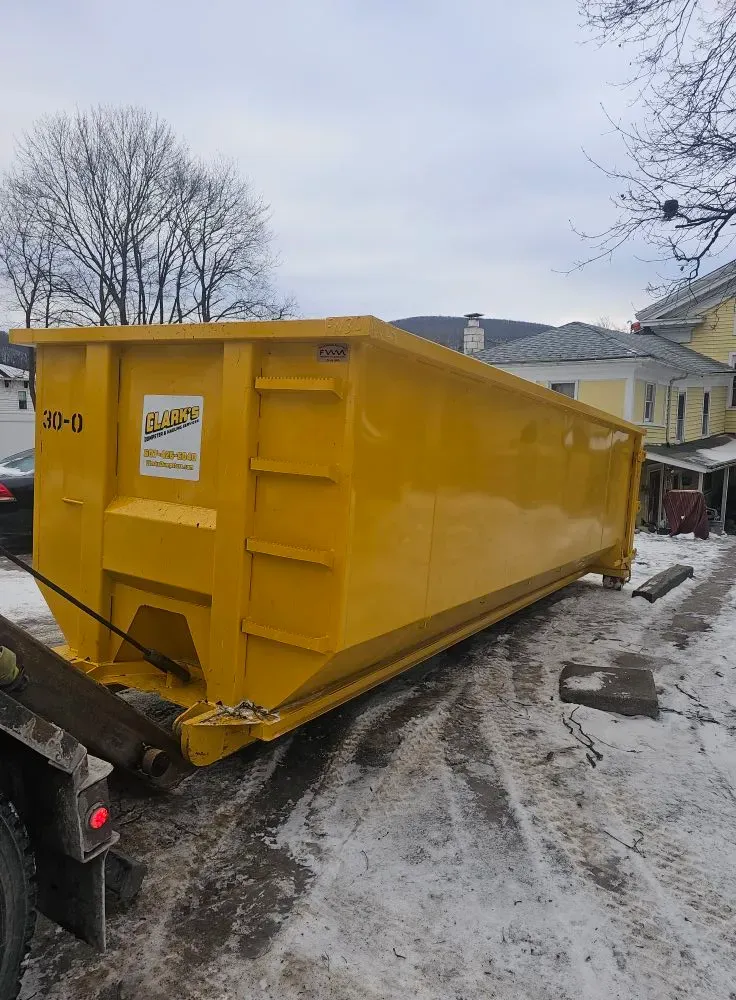 A large yellow dumpster is sitting in the snow in front of a house.