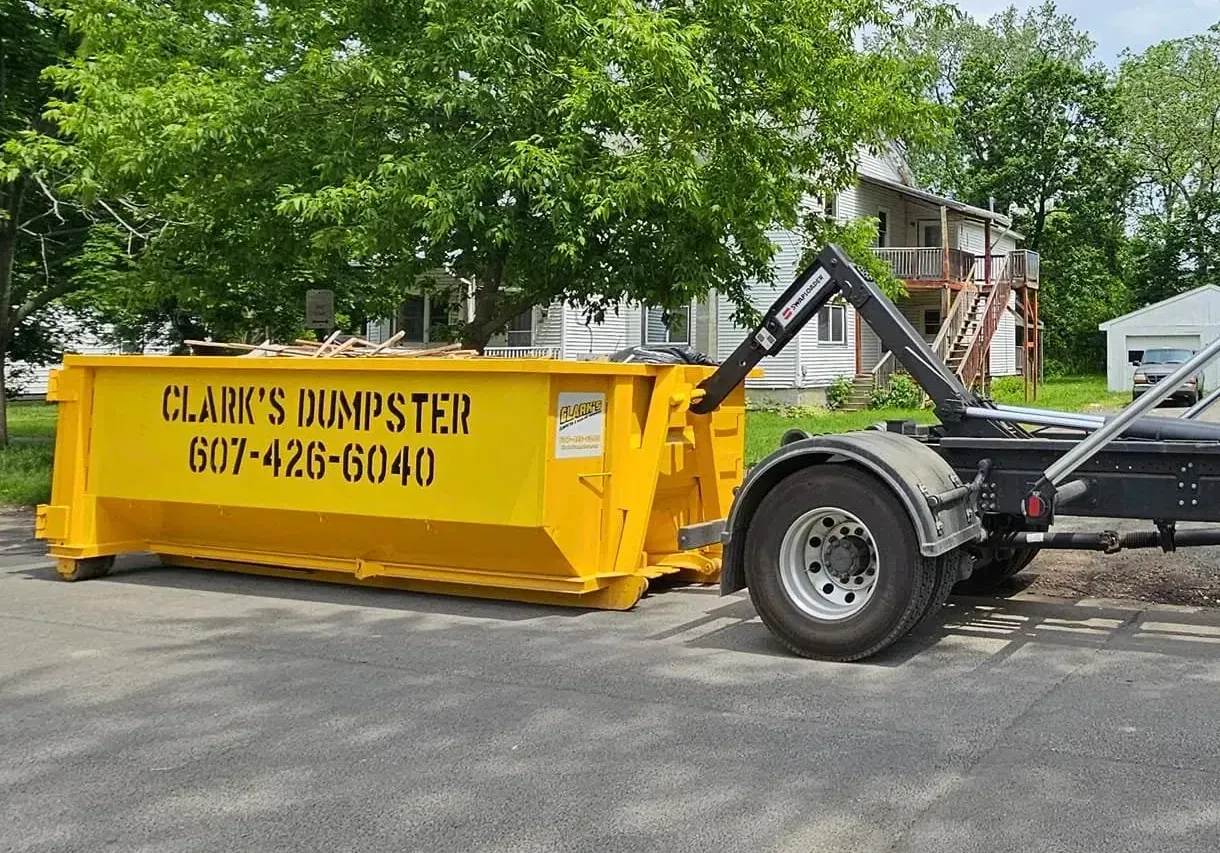 A yellow dumpster is sitting on the side of the road next to a truck.