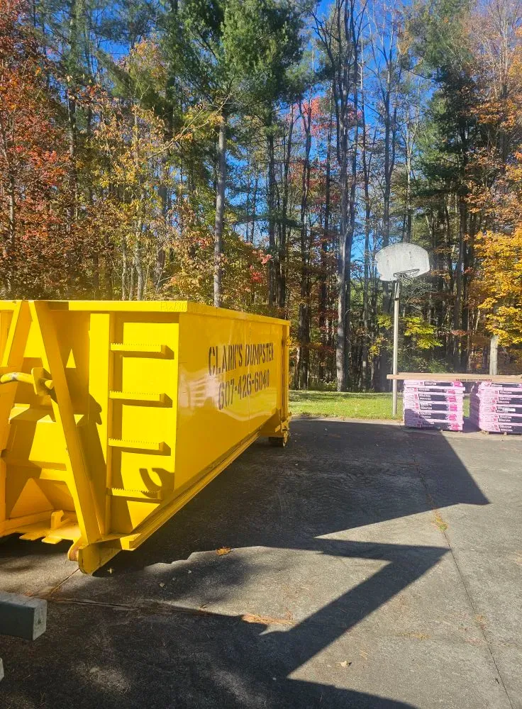 A large yellow dumpster is parked in front of a basketball court.