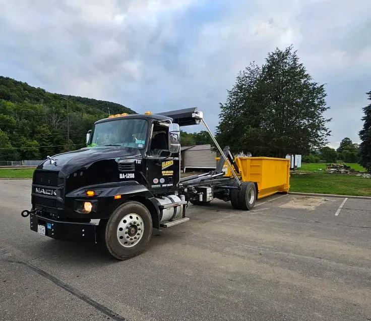 A dump truck with a yellow dumpster attached to it is parked in a parking lot.