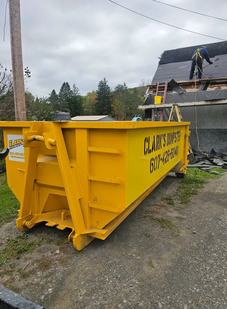 A large yellow dumpster is parked in front of a house under construction.