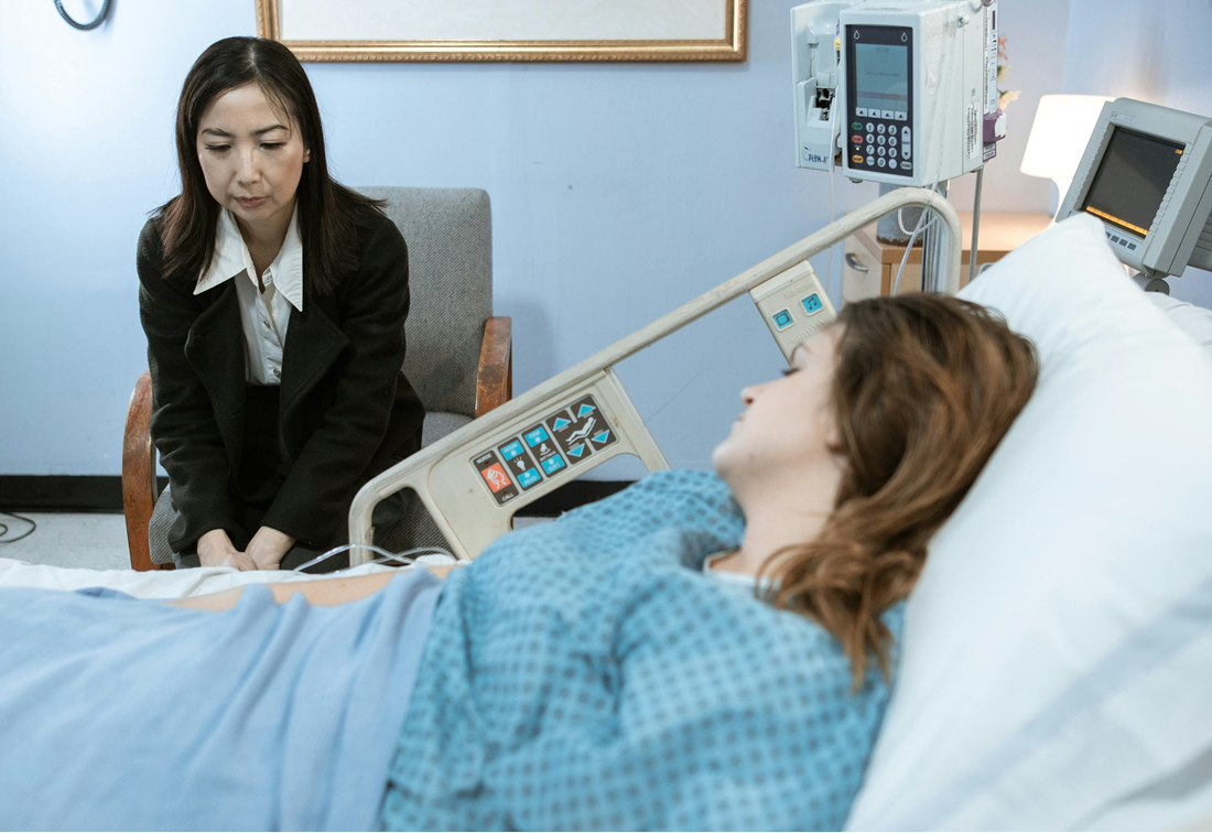 Woman visiting a patient in a hospital room beside a bed and medical equipment
