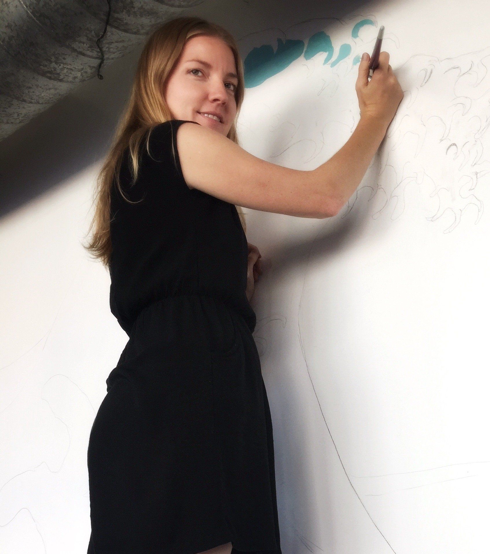 Woman in black dress drawing on a wall, smiling, with a partially drawn blue design.
