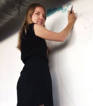 Woman in black dress painting on a white wall.
