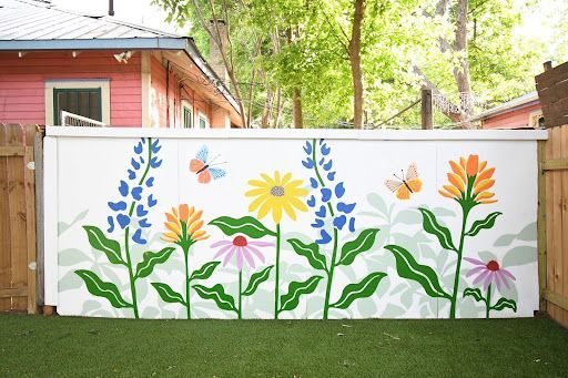 White fence mural with colorful painted flowers and butterflies.