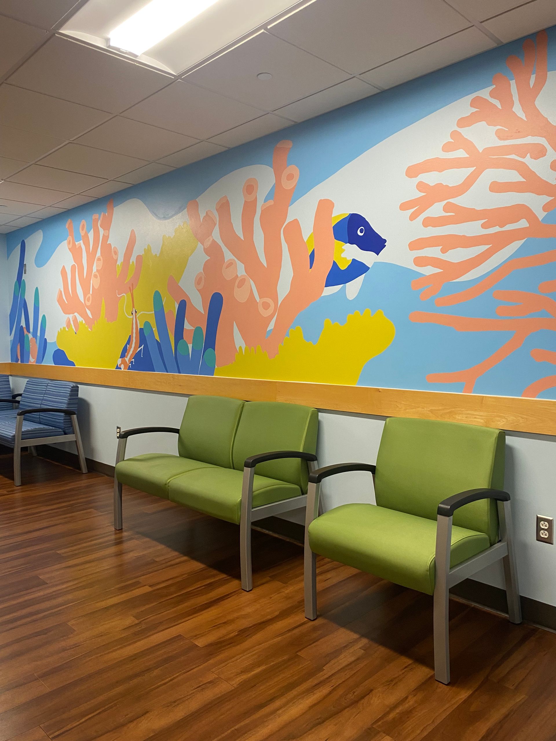 Long coral reef mural with a reef fish above the seating in the pediatric waiting room at Dell Children's, Austin TX