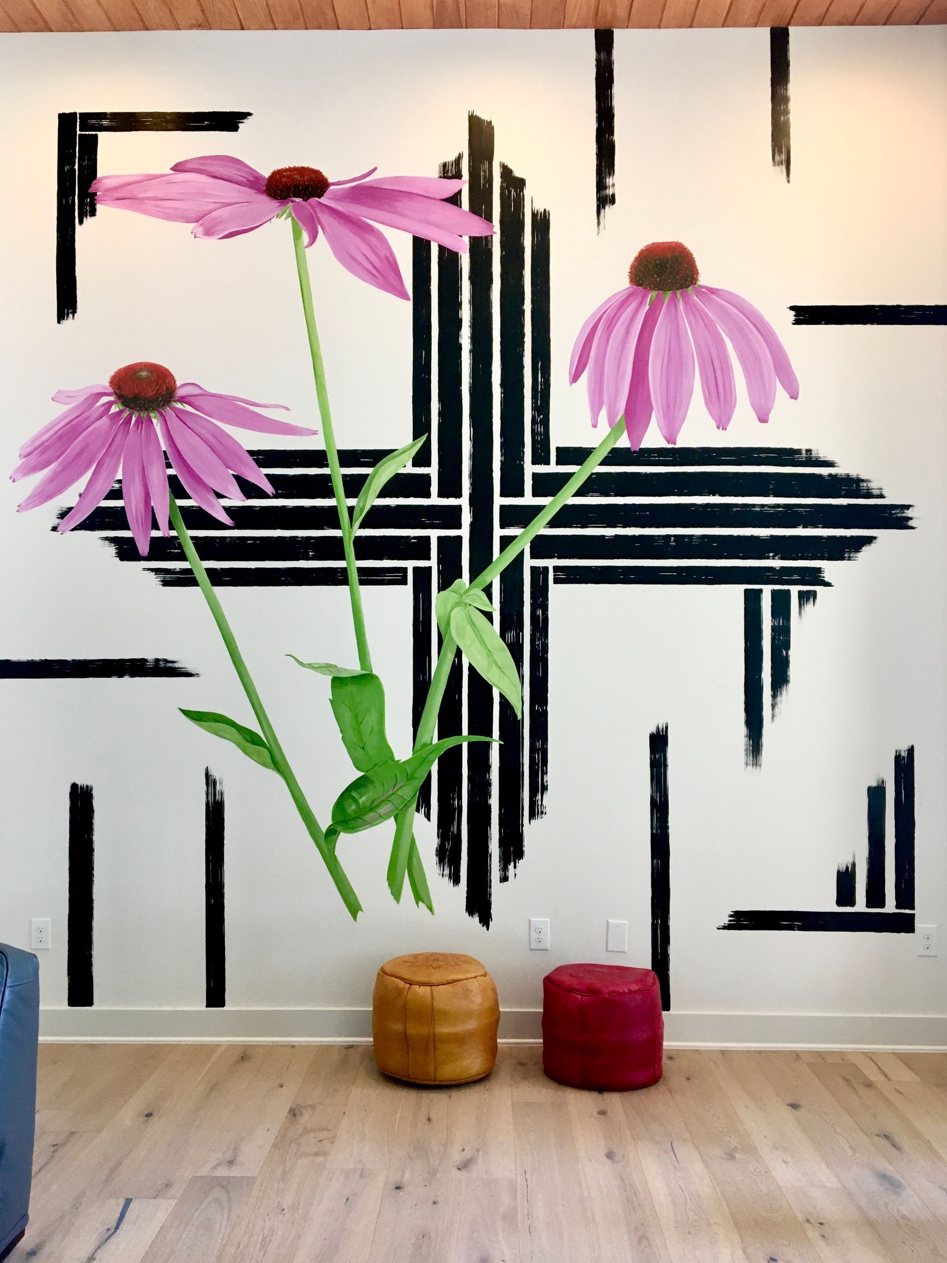 Mural of large pink flowers with black geometric lines on a white wall. Two wooden stools sit below.