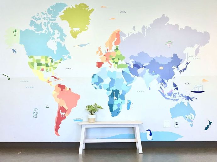 Colorful world map mural on a white wall, a small white table with a plant is in front of it.
