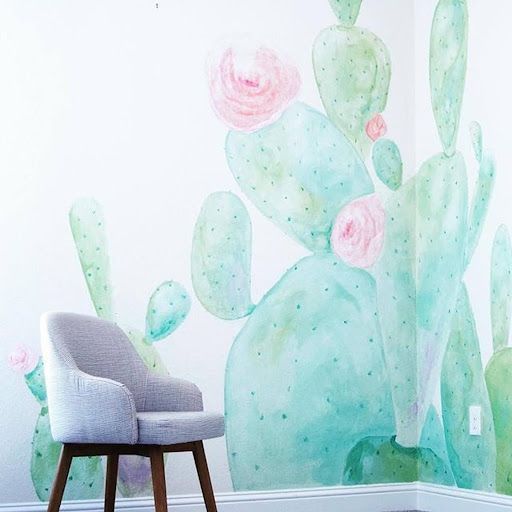 Gray armchair in front of a wall mural of watercolor cacti and pink flowers.