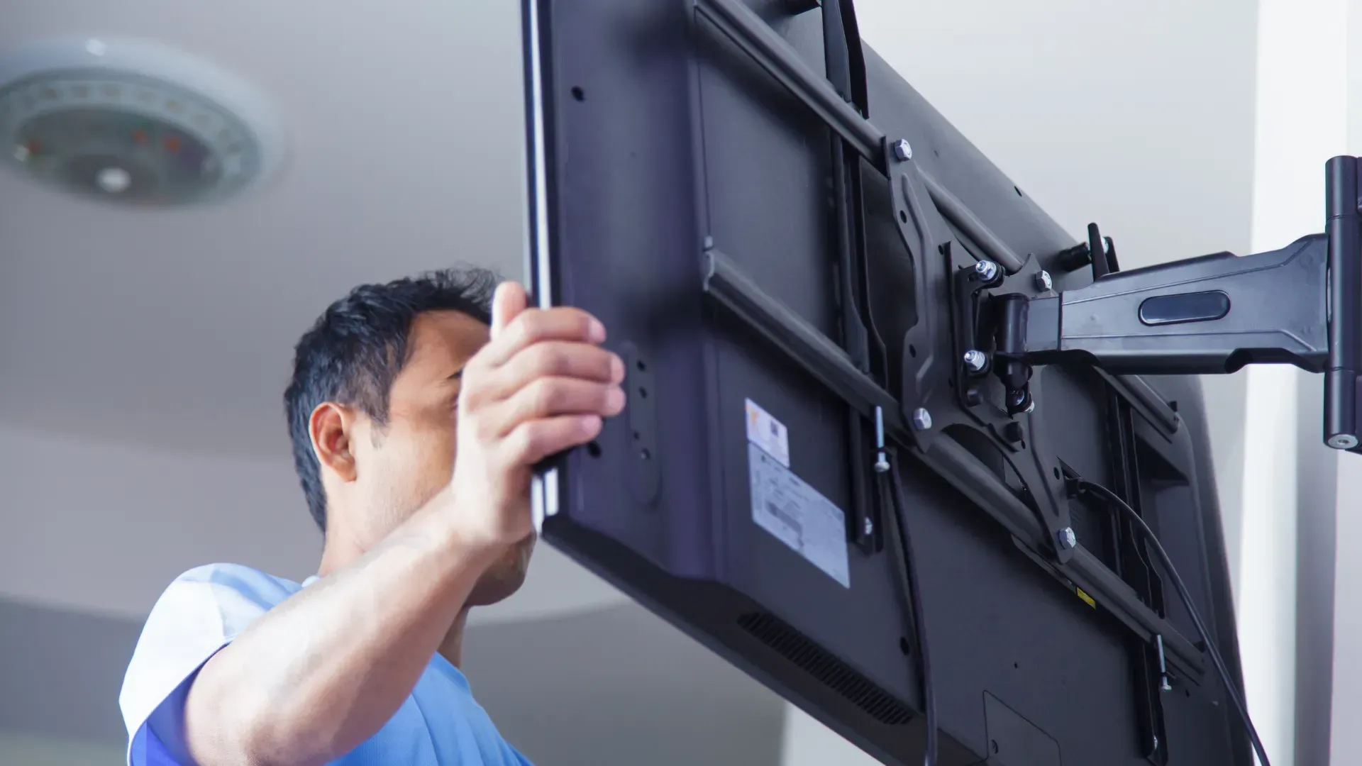 Man mounting a large black TV on a wall bracket, indoors.