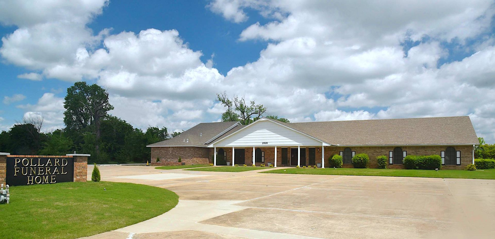 A single-story brick building with a covered entrance, a curved driveway, and a cloudy blue sky.