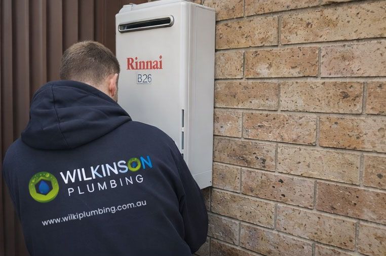 Wilkinson plumber installing a Rinnai water heater on a brick wall.