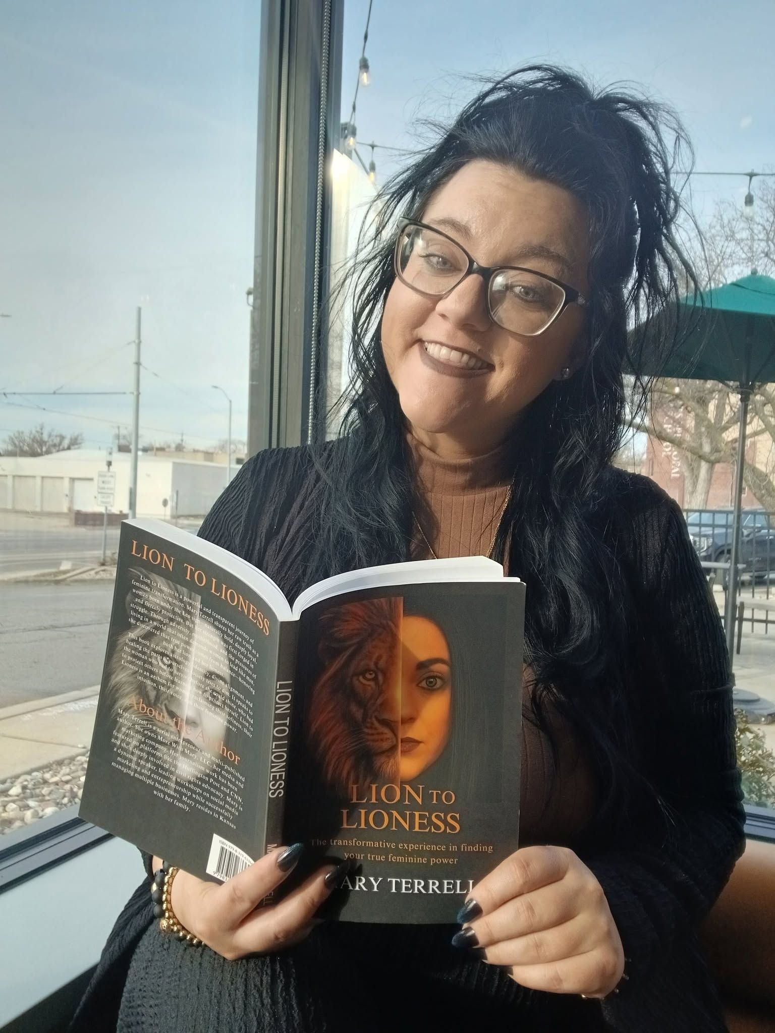 Woman smiling and holding an open book by a window with water in the background