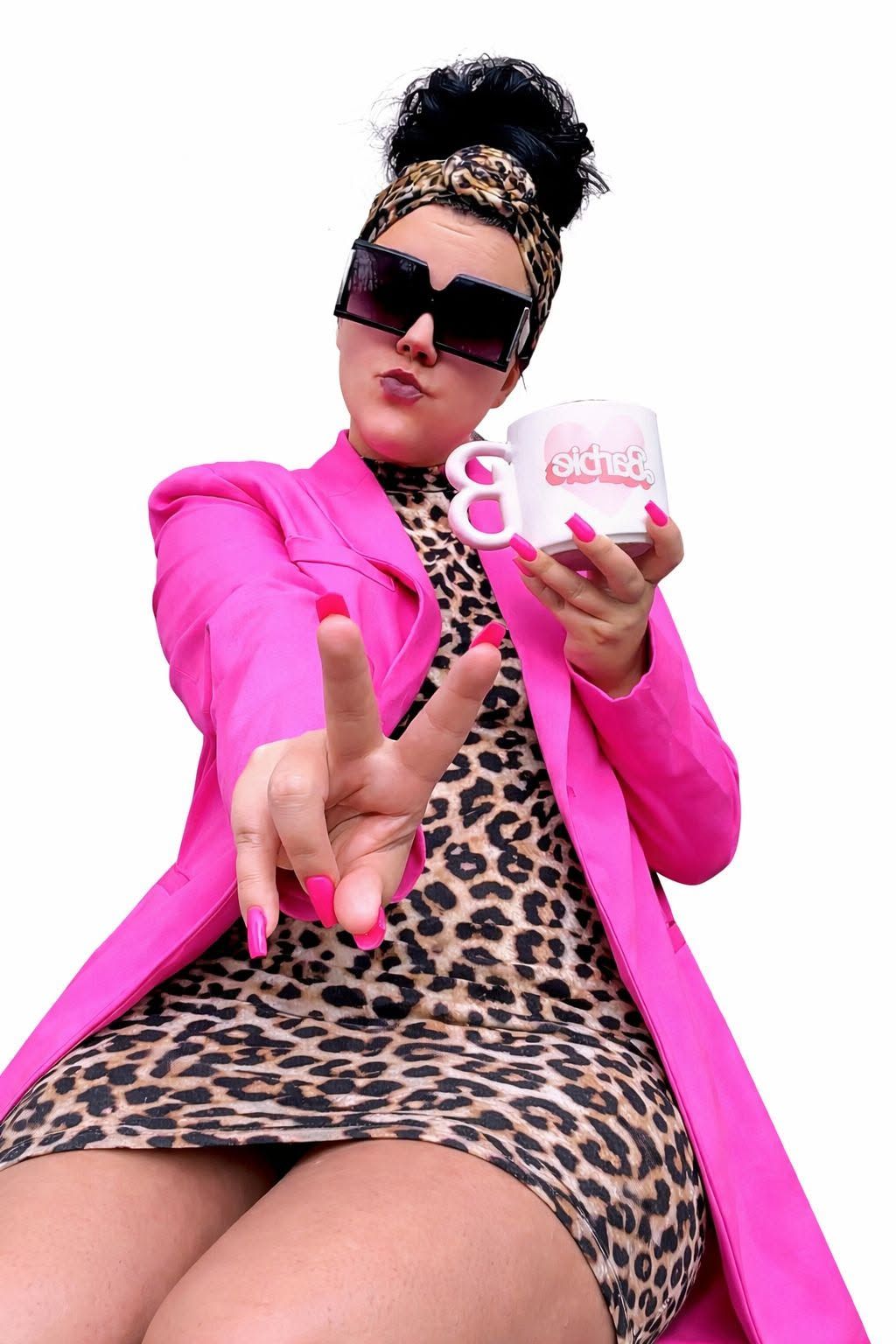 Person in a pink coat and leopard dress, holding a mug and reaching toward the camera