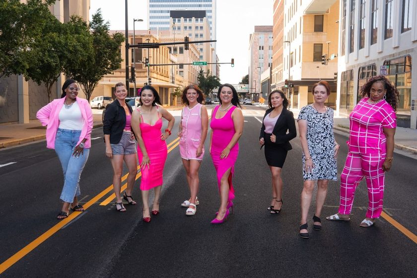 Seven people in bright pink and patterned outfits walk together on a city street.