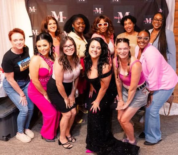 Group posing in front of a branded backdrop, smiling and leaning together at an event