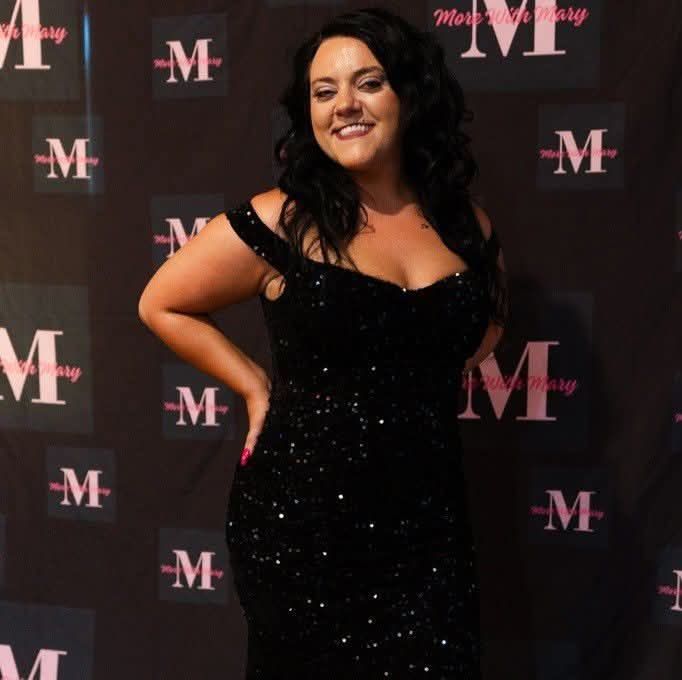 Woman in a black sequined dress smiling at a step-and-repeat event backdrop