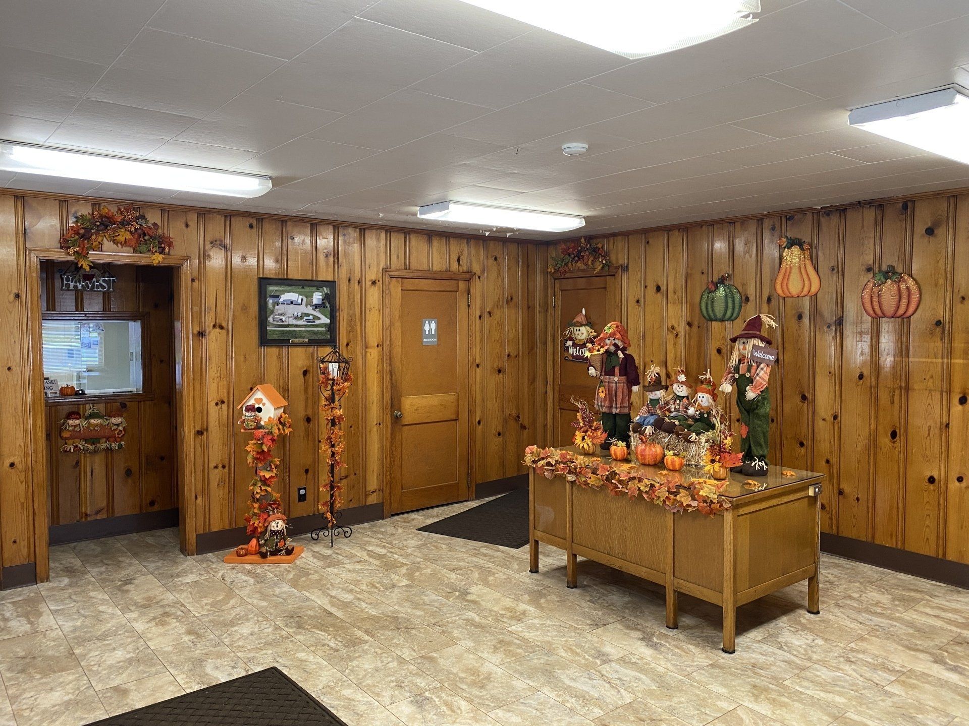 A lobby with wood-paneled walls and fall-themed decor, including decorative pumpkins and figures on a wooden desk.