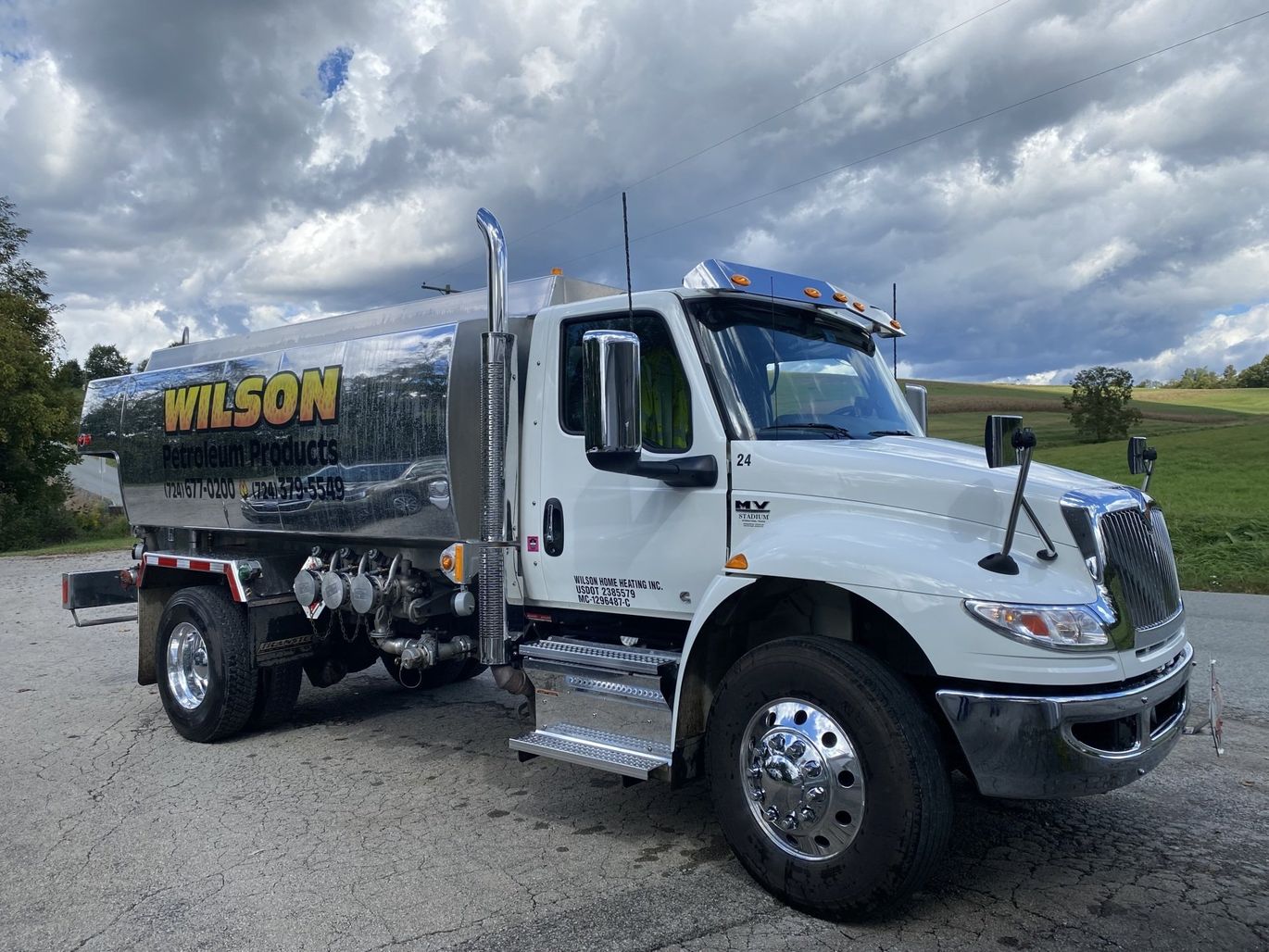 A white Wilson commercial fuel tanker truck parked on a gravel lot under a cloudy sky.